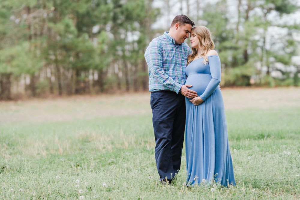 Sweet maternity portrait of a couple in blue and plaid standing together in a sunny meadow.