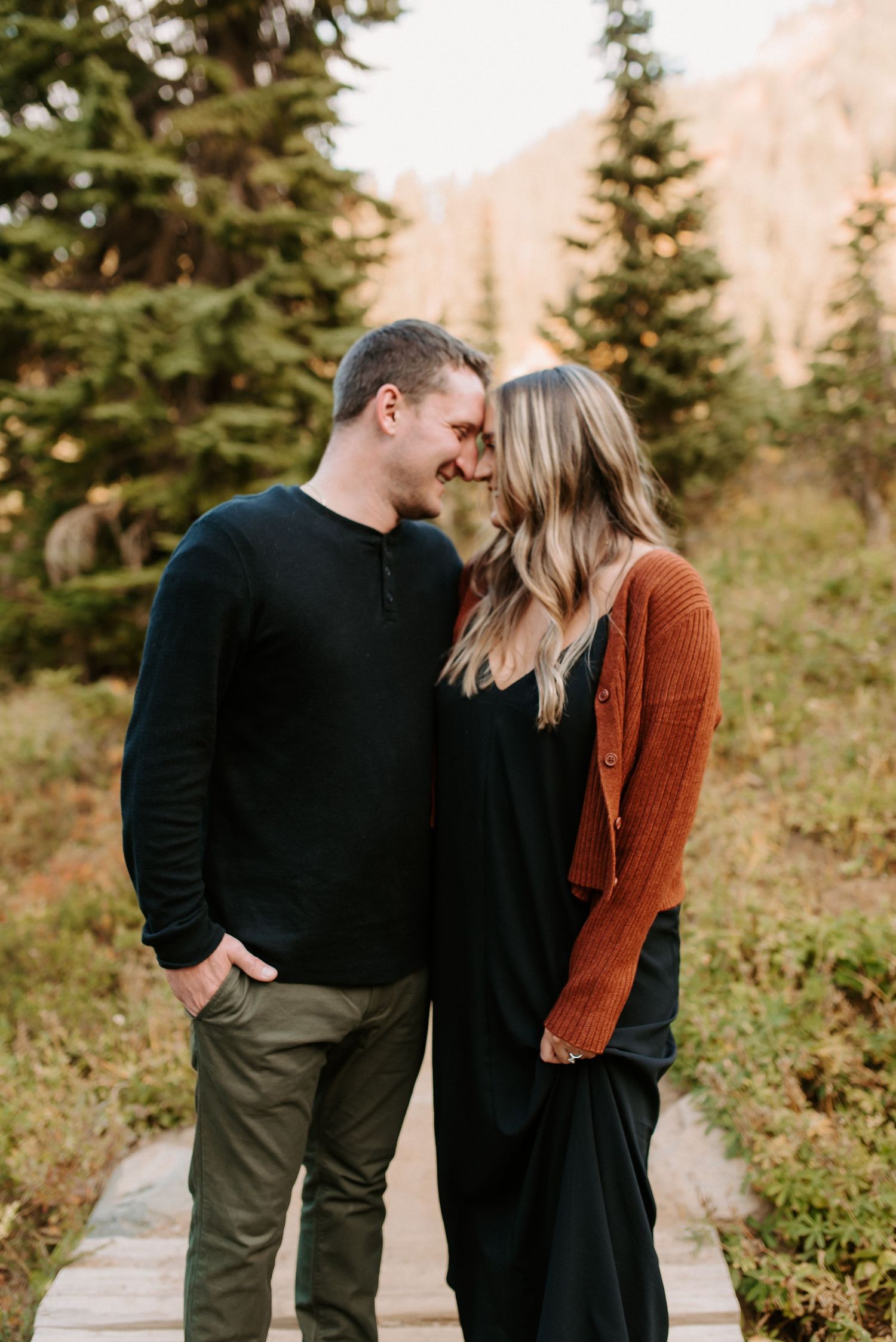 Couple in casual fall outfits sharing tender moment against mountain backdrop.