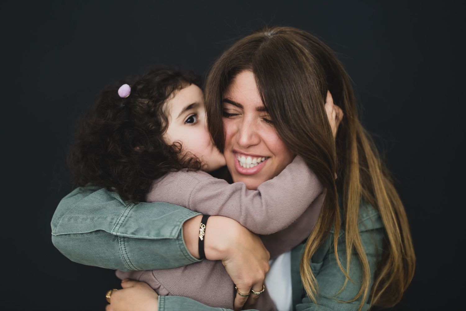 Heartwarming candid moment of parent and child embracing and laughing against dark background.