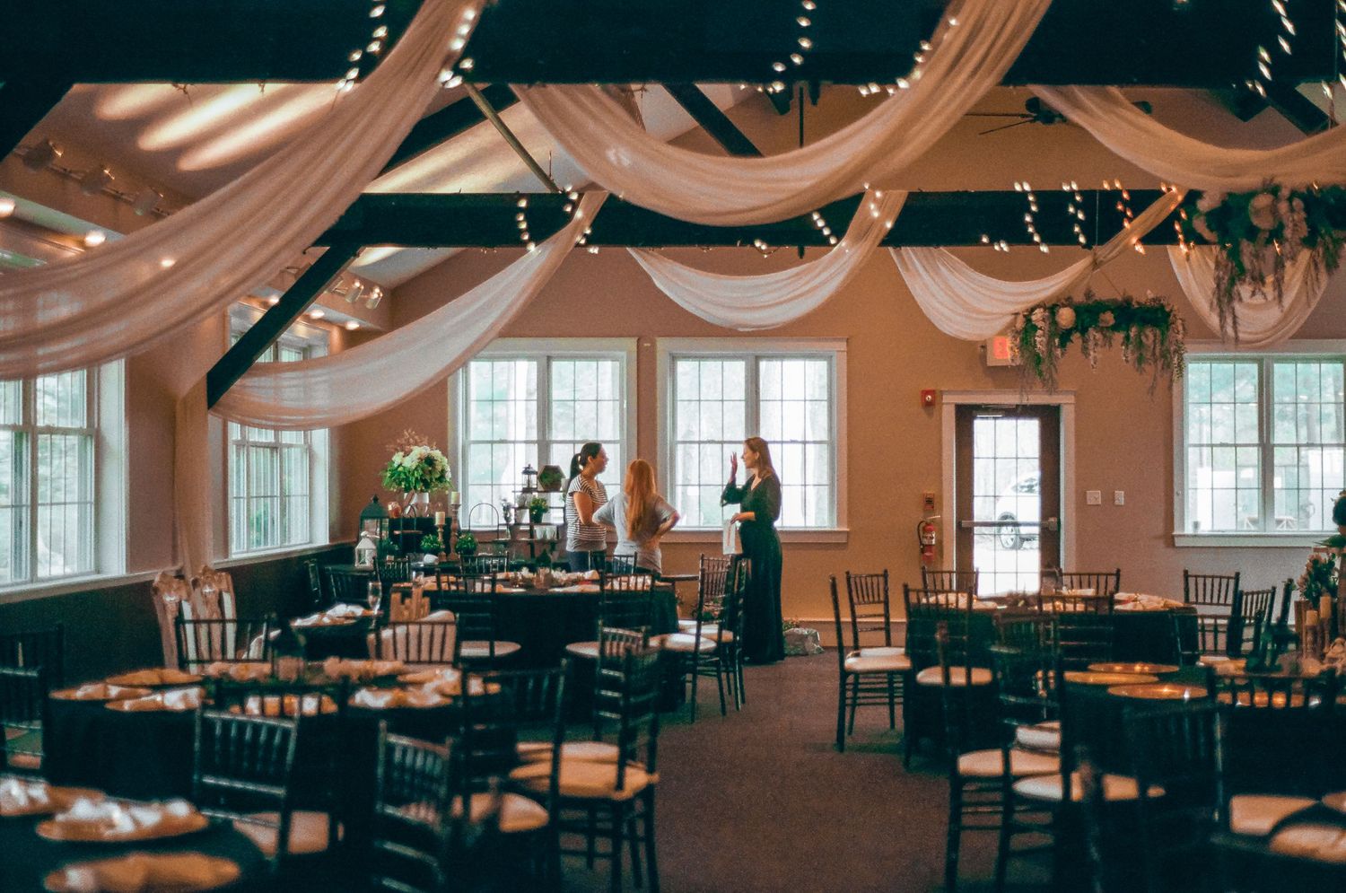 An elegant reception venue with draped fabric decor and wooden chairs set up for a wedding celebration.