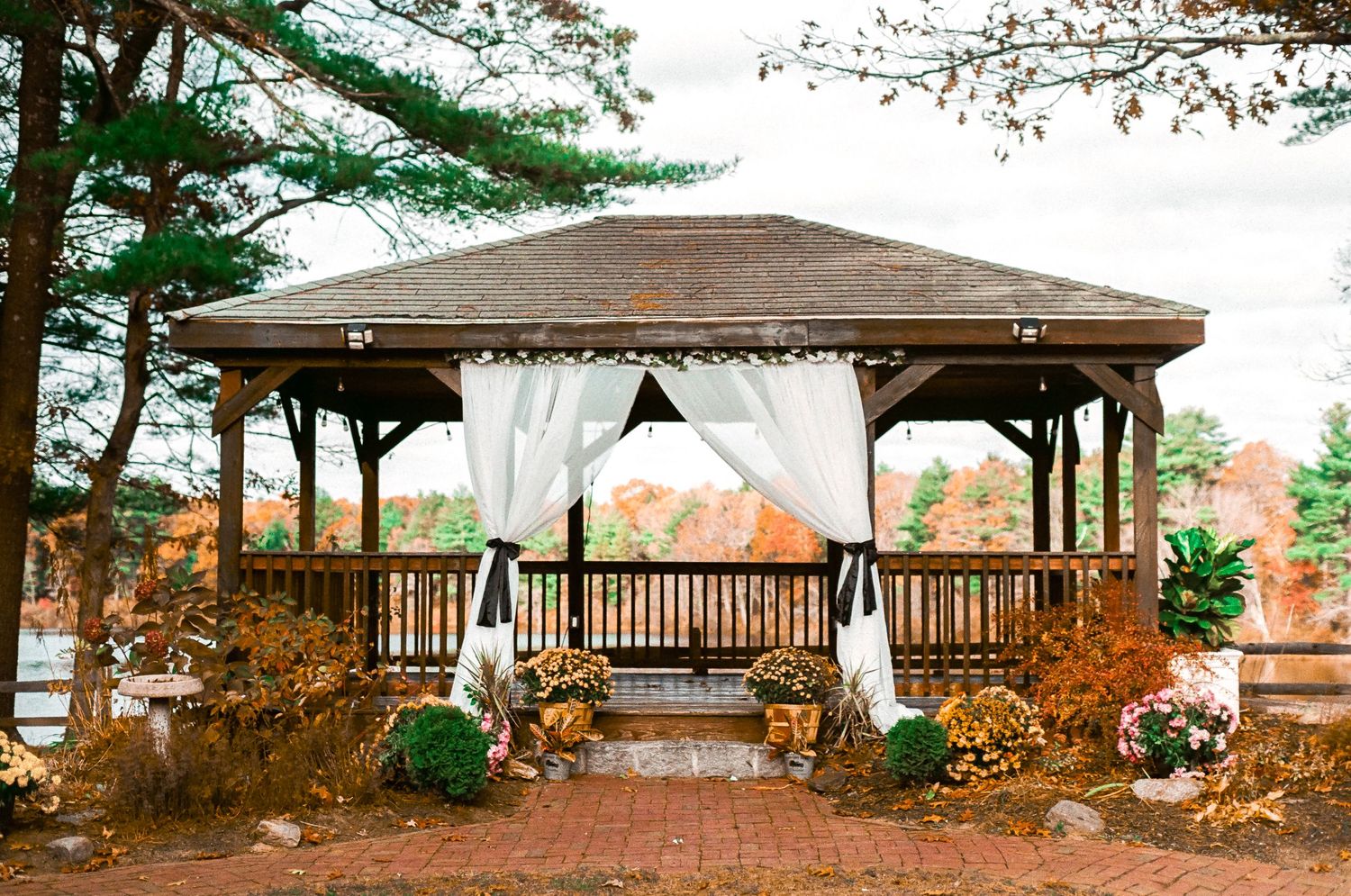 Wedding gazebo with white drapes and autumn decorations set against a scenic outdoor backdrop.