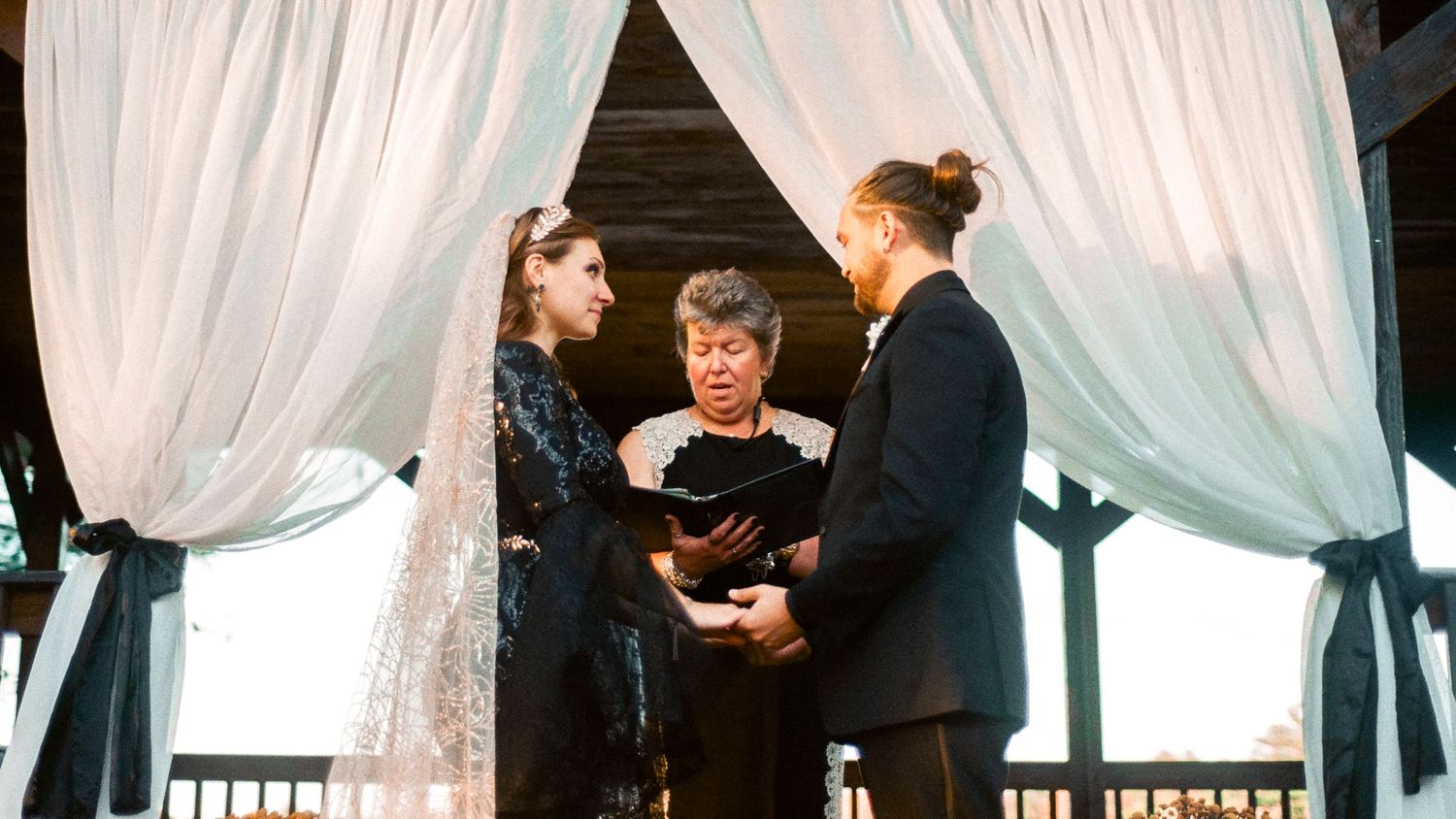 Wedding ceremony in progress beneath a white-draped gazebo with autumn decorations.