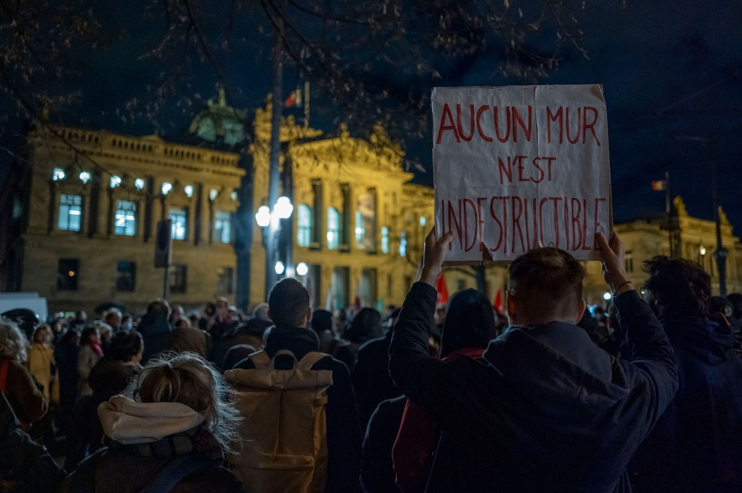 Nighttime protest gathering outside historic building with illuminated facade.