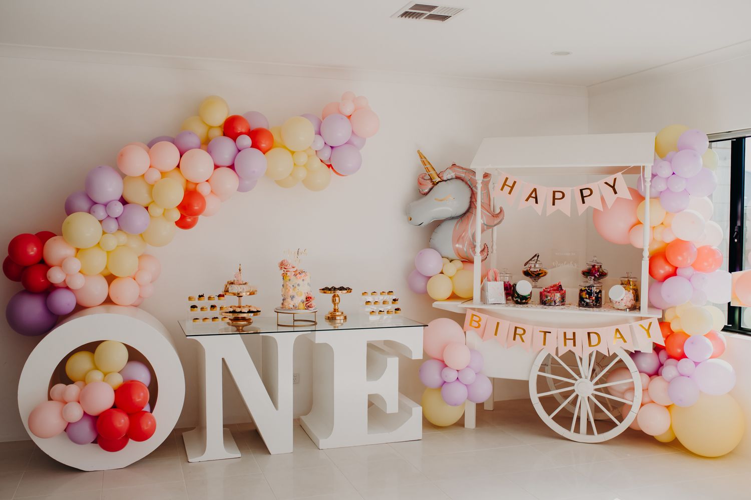 Whimsical birthday party setup with pastel balloon arch and ONE letters in white.