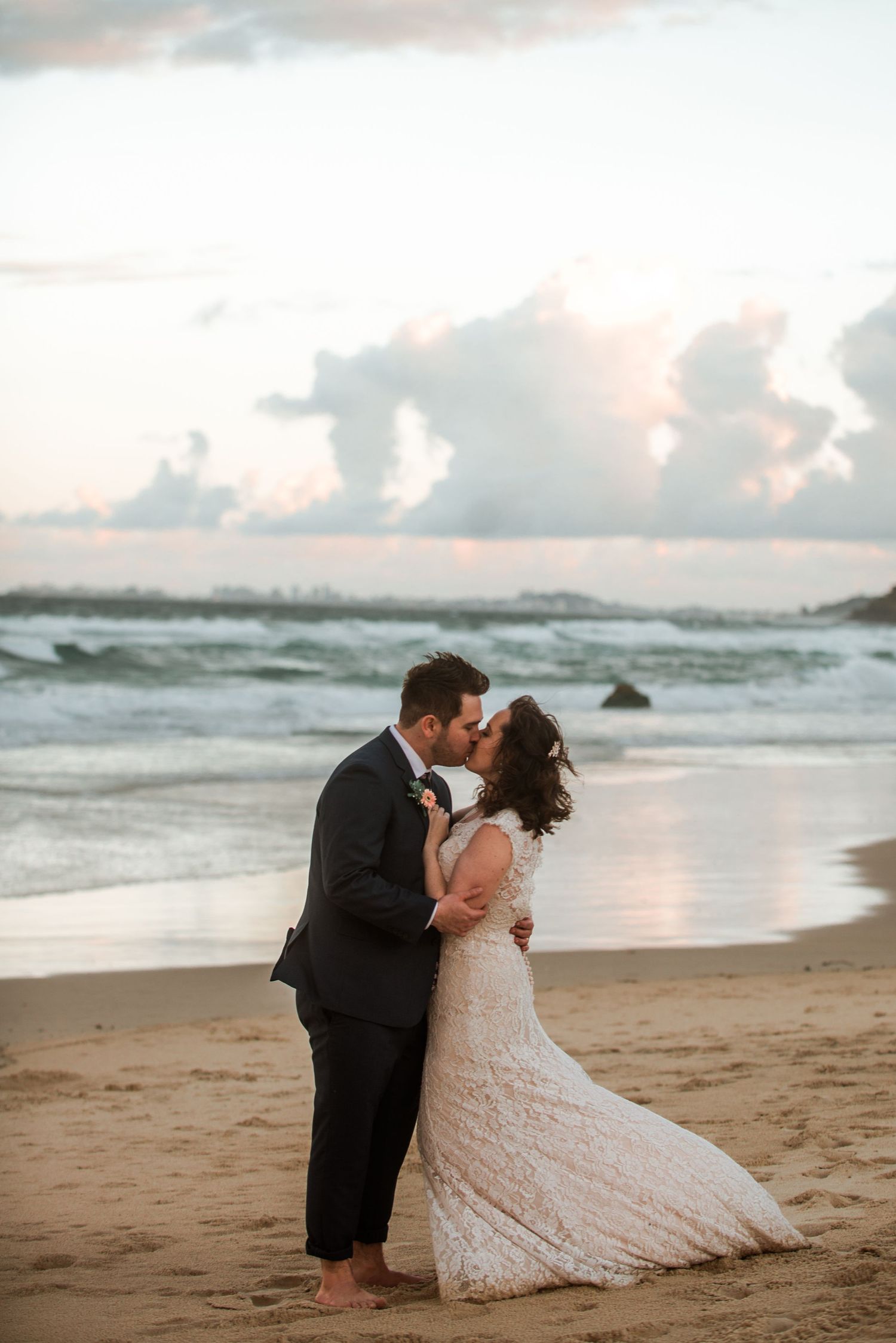 A romantic sunset beach wedding photo showing a couple embracing in formal attire on the sandy shore.
