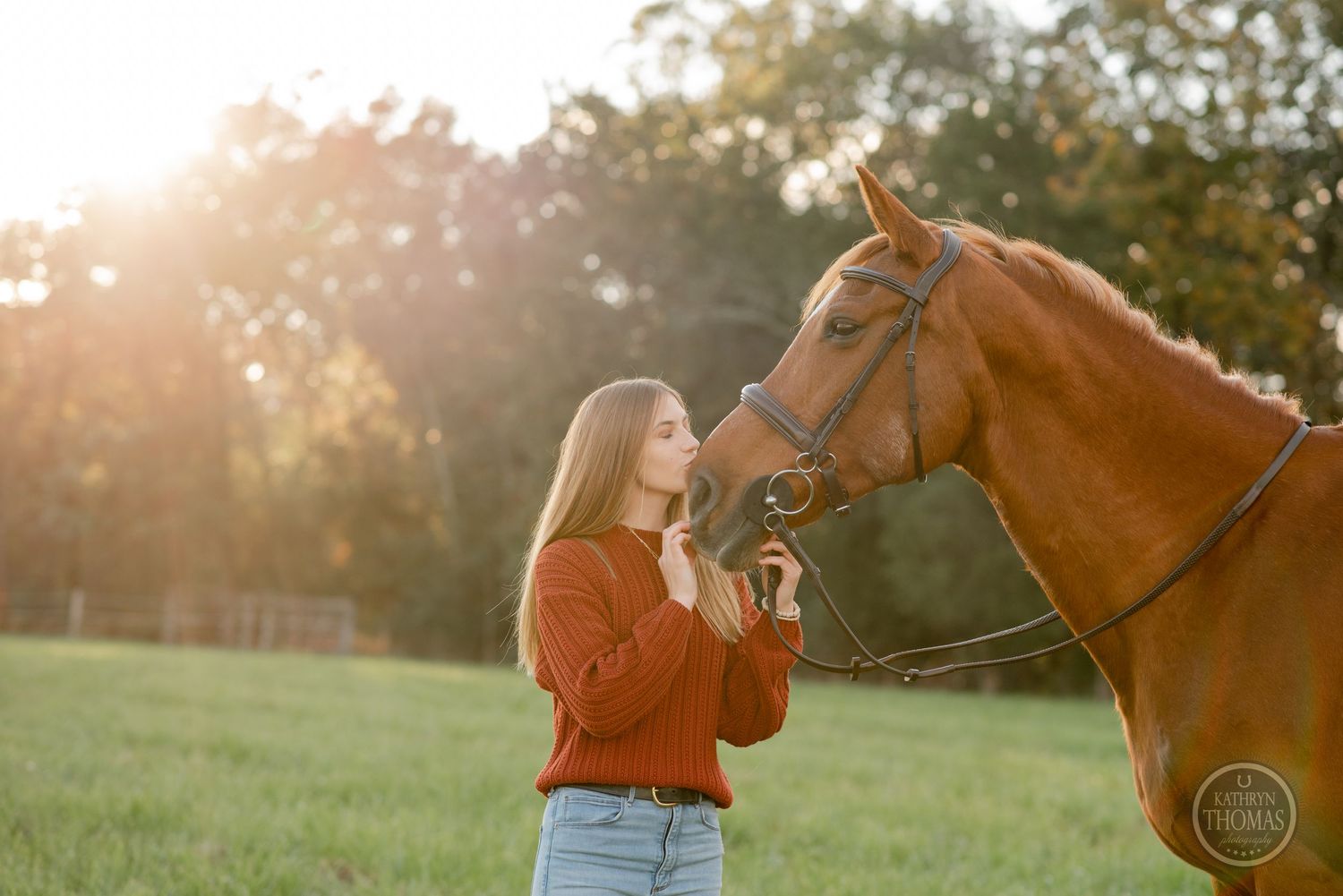 Chestnut horse and rider share tender moment in sunlit field during golden hour.