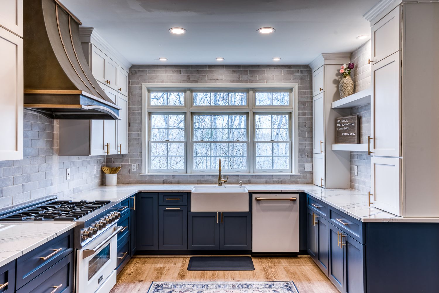 Modern kitchen with navy blue cabinets, white countertops, and a large window overlooking the backyard.