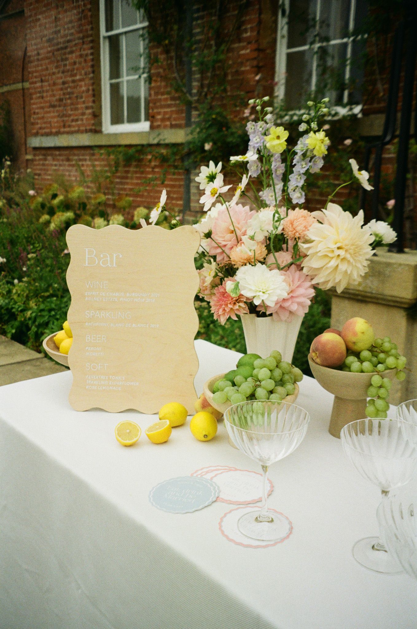 Wedding bar menu display with fresh flowers and fruit on white tablecloth.