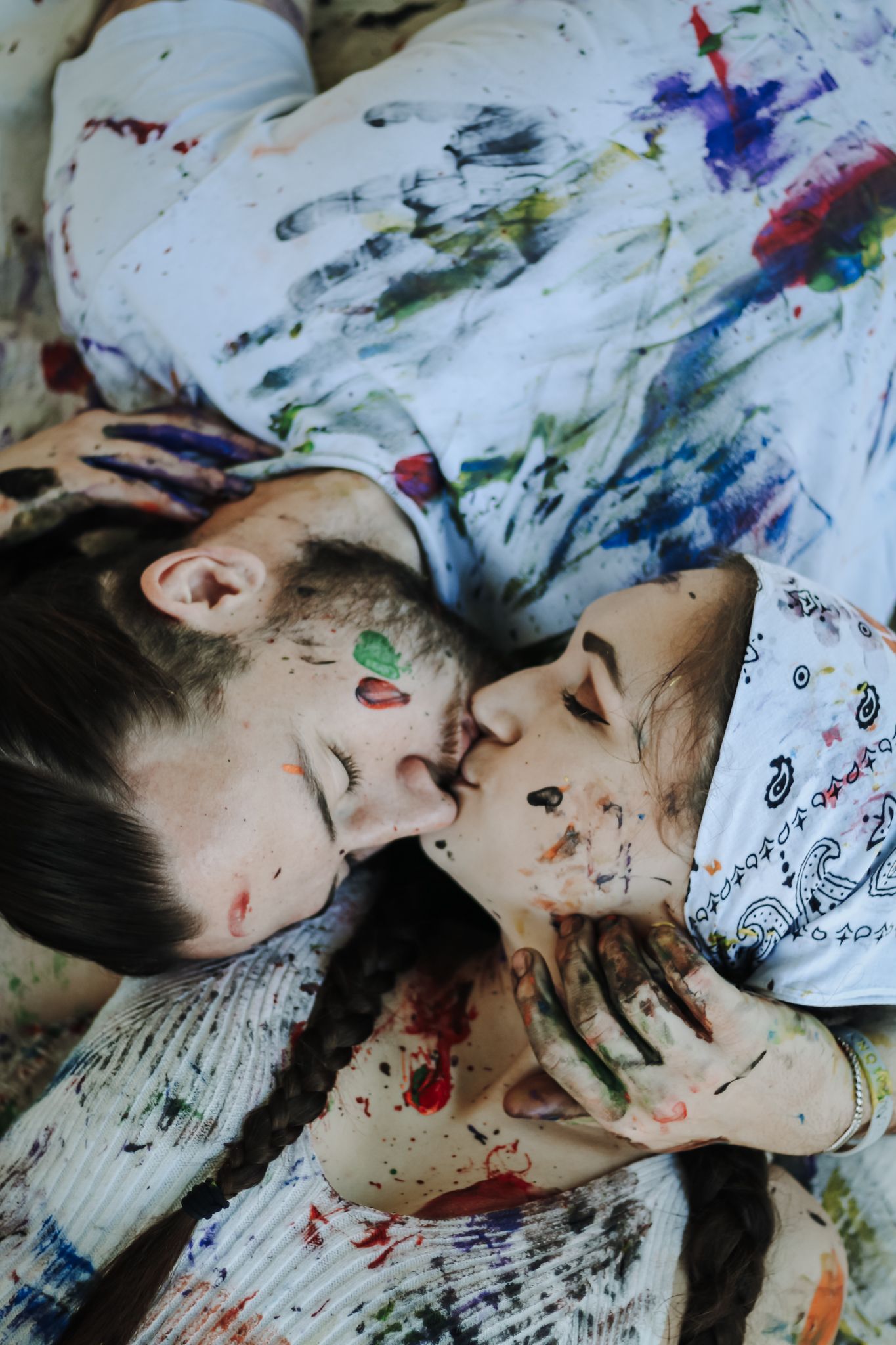 Two people lying down covered in colorful paint splatters in an artistic portrait.