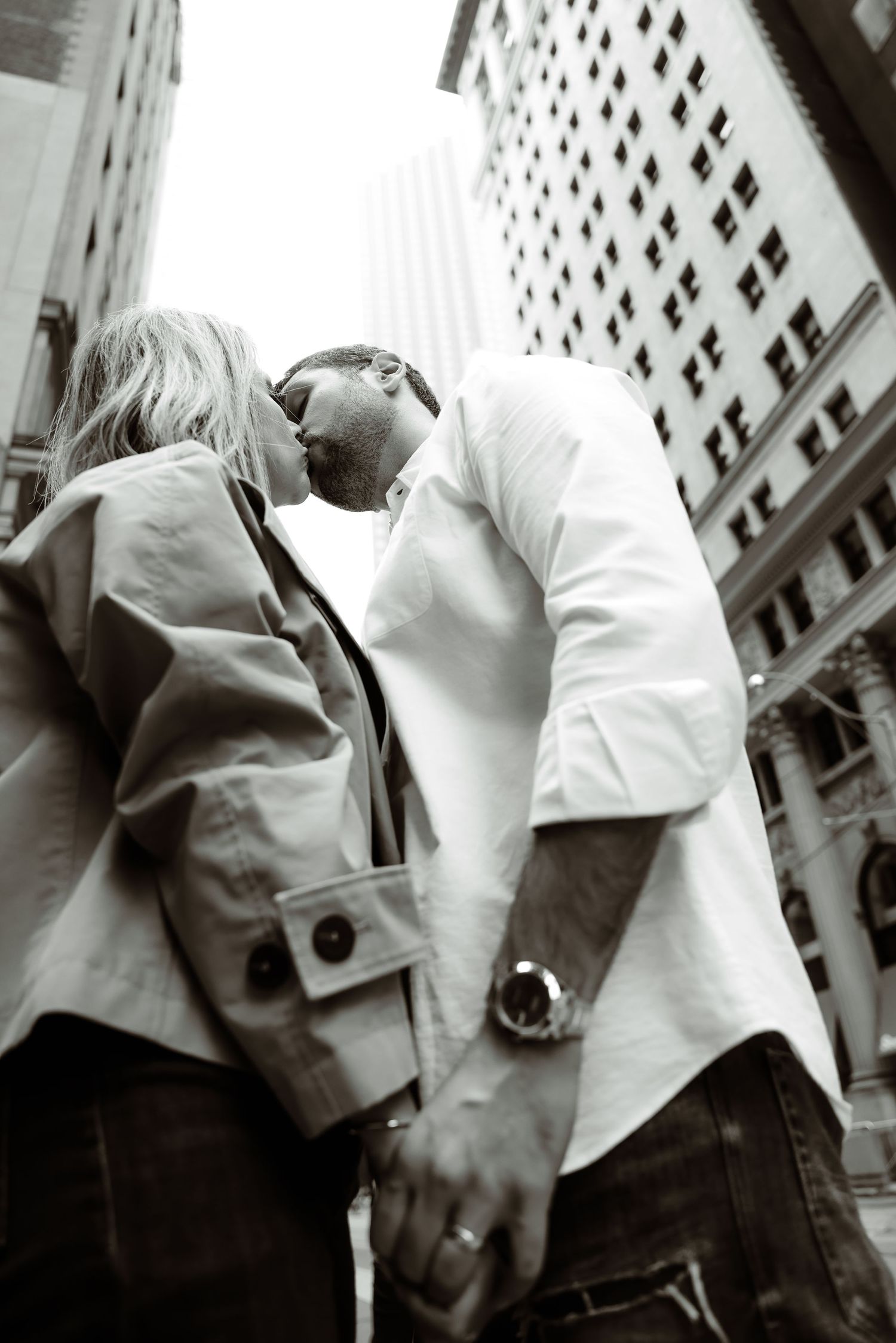 Black and white romantic portrait of a couple embracing against an urban backdrop of tall buildings.
