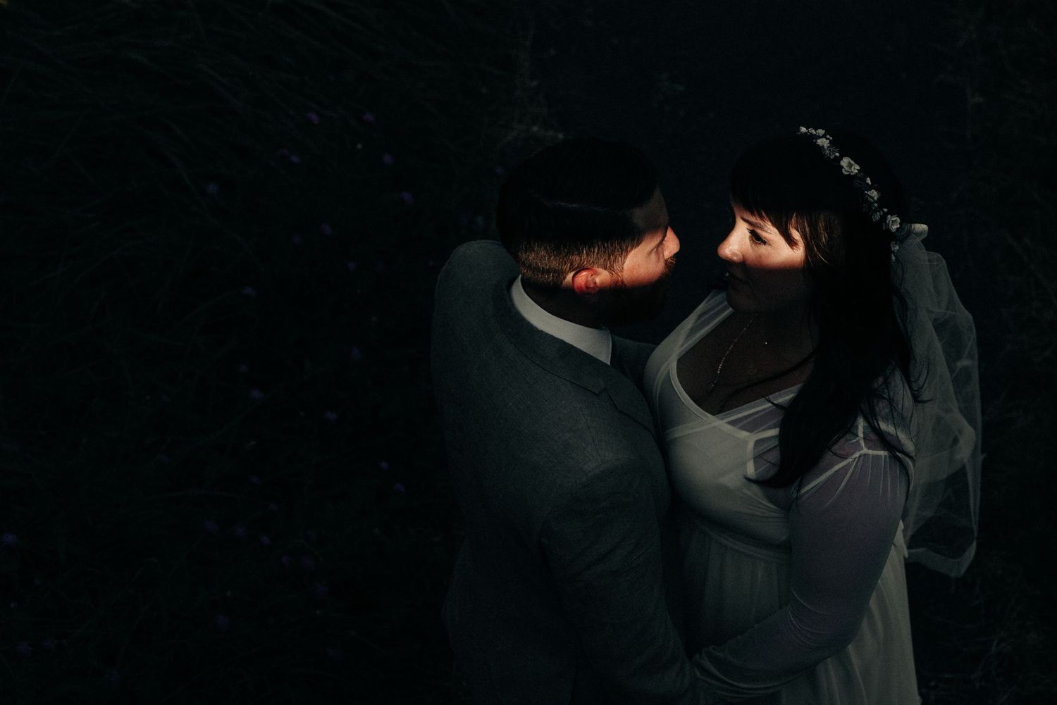 Intimate dark portrait of a couple embracing in shadows creating a moody romantic atmosphere.