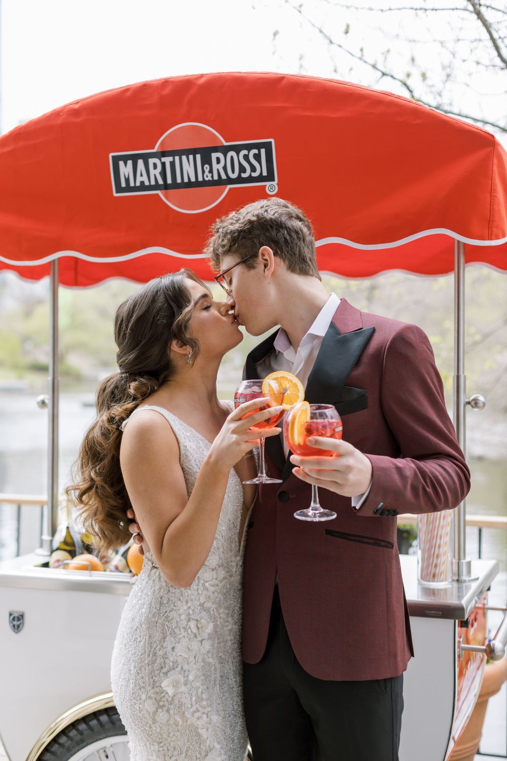 Wedding couple sharing cocktails under a red Martini & Rossi umbrella on an outdoor patio.