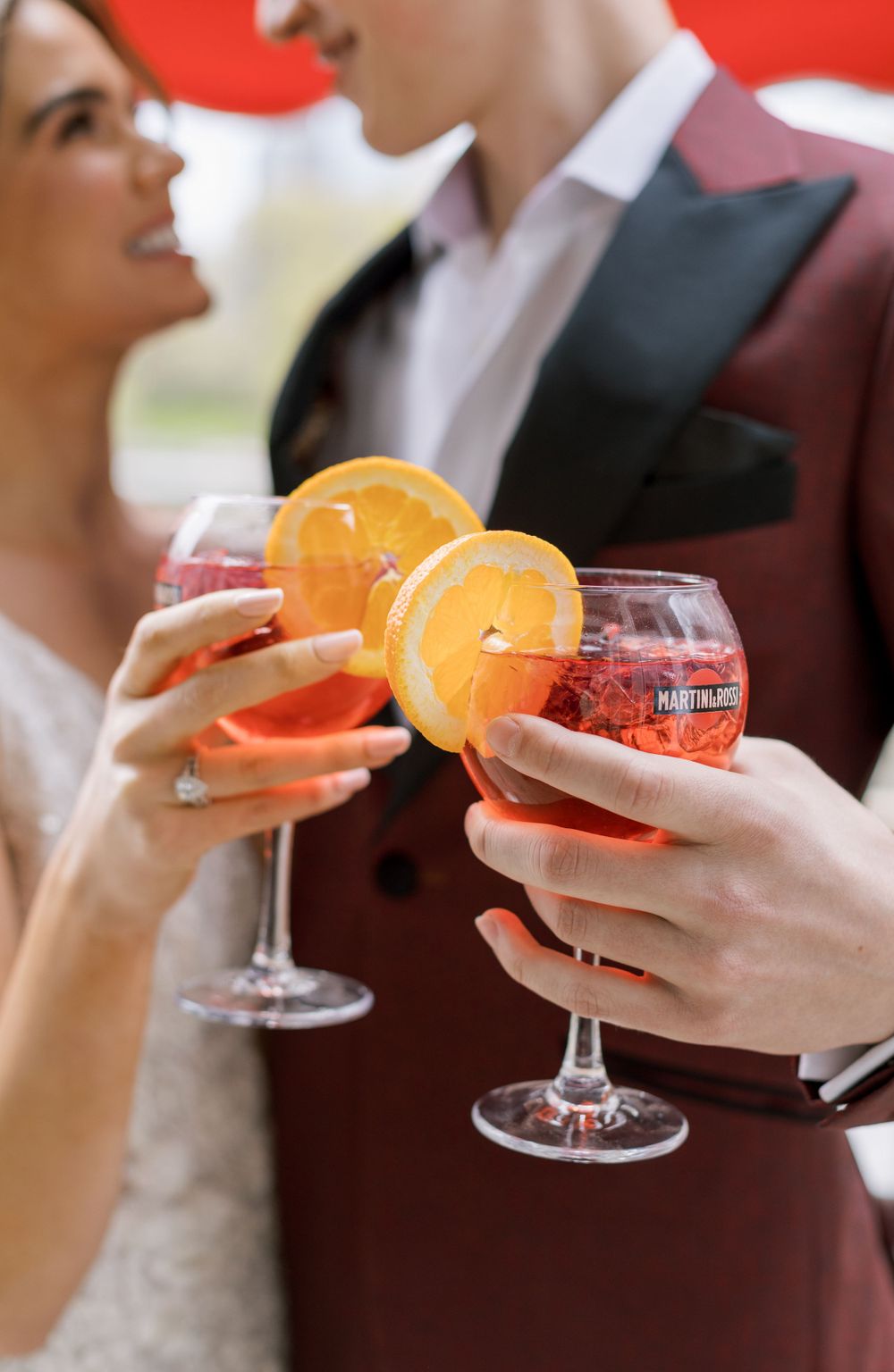 Close-up of hands holding orange garnished cocktails during a wedding celebration.