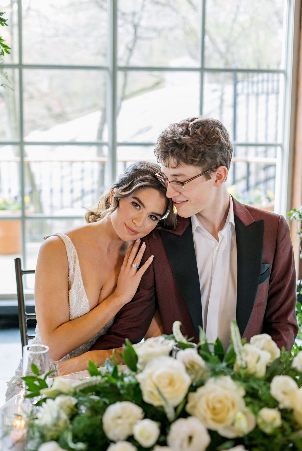 Elegant wedding couple sharing an intimate moment at a table decorated with white roses.
