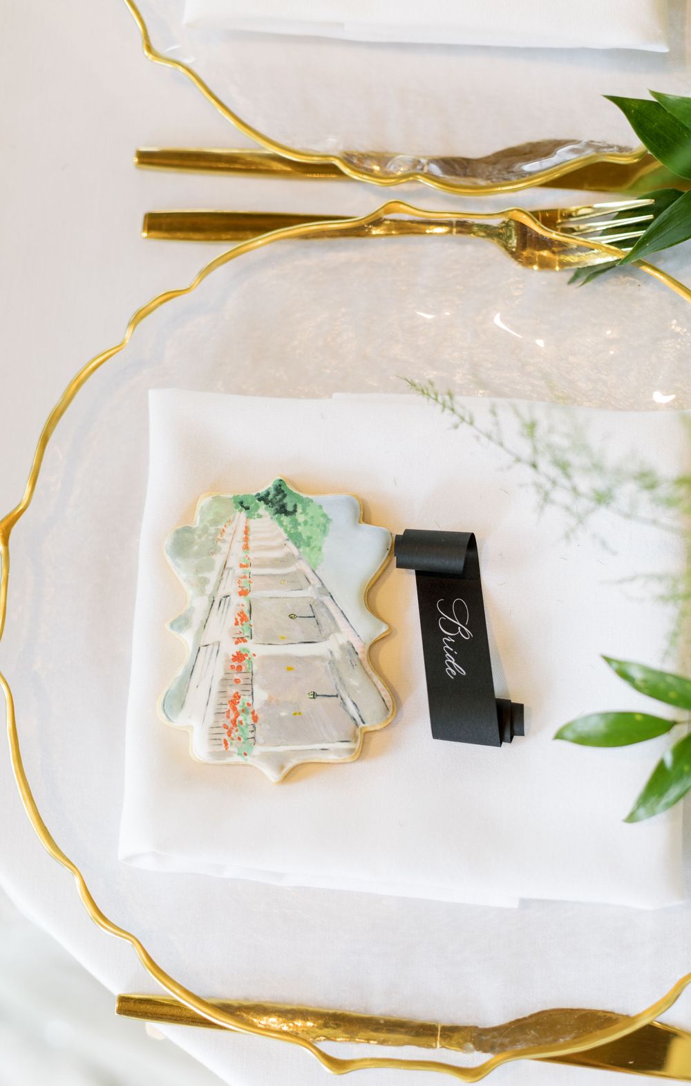 Decorative wedding favor cookie with watercolor design and black ring box on white plate.