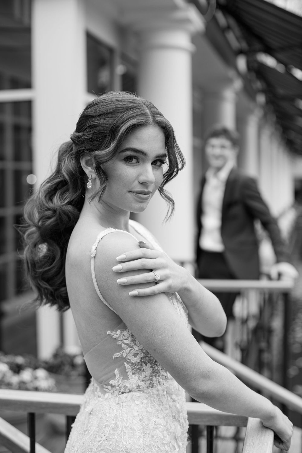Black and white portrait of bride in lace dress with elegant curled hairstyle on venue balcony.