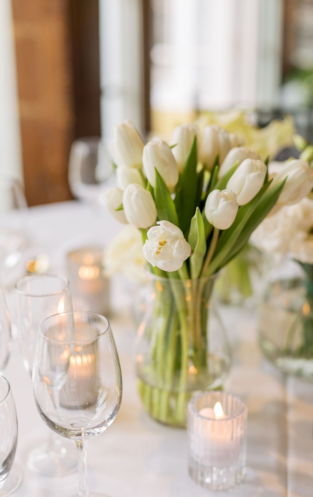 Elegant white tulips in clear vase with lit candles on wedding reception table.