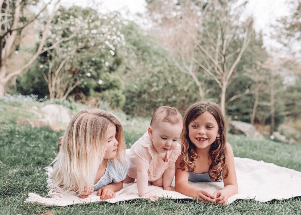 Candid outdoor photo of children lying on a blanket in a grassy area on a sunny day.