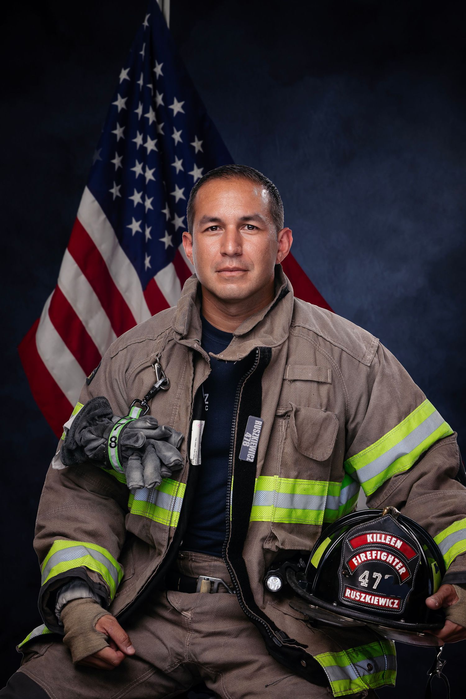 Firefighter in uniform posing with American flag and helmet.