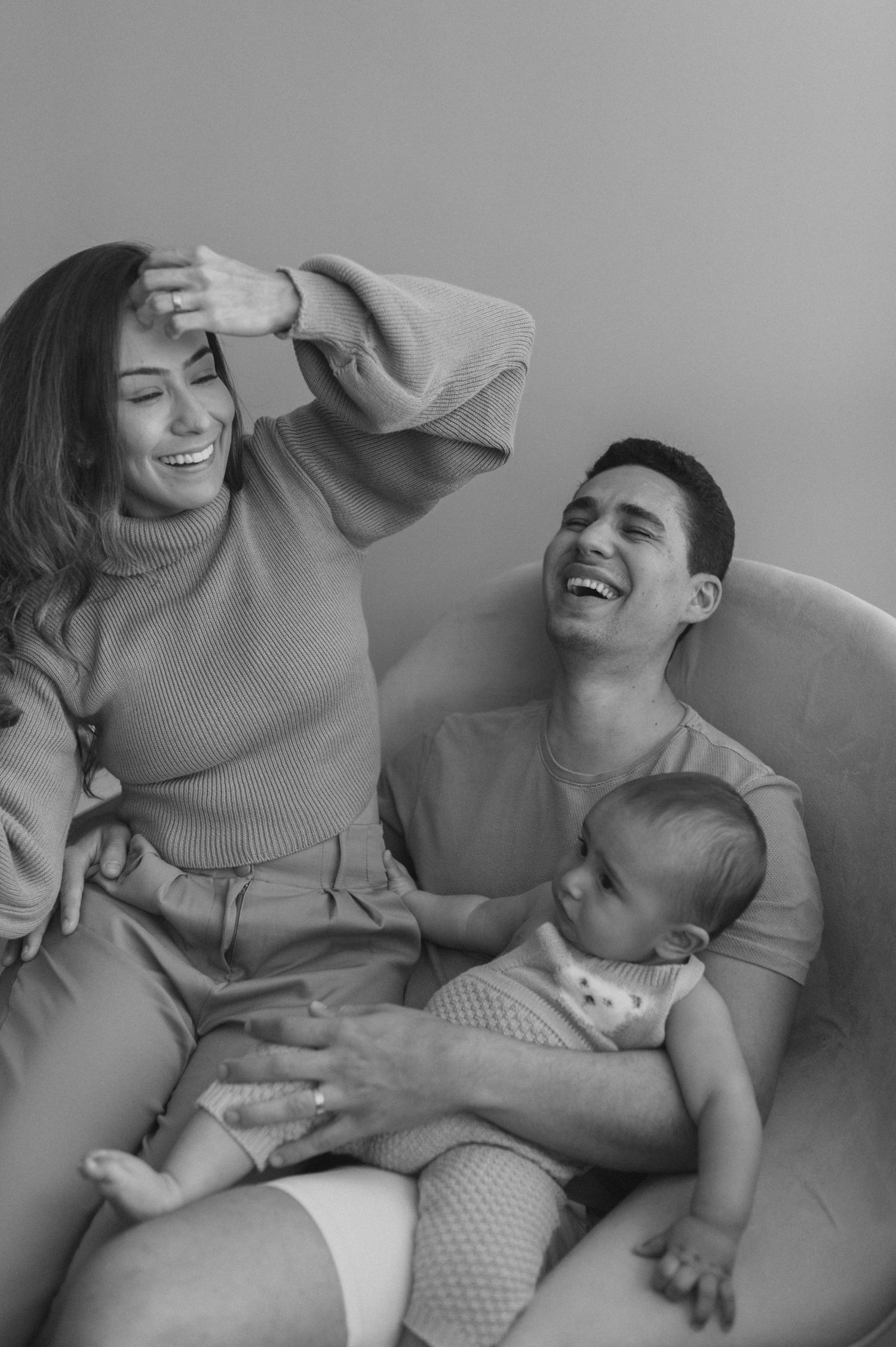A candid black and white family photo showing joyful laughter while relaxing on a couch with a baby.