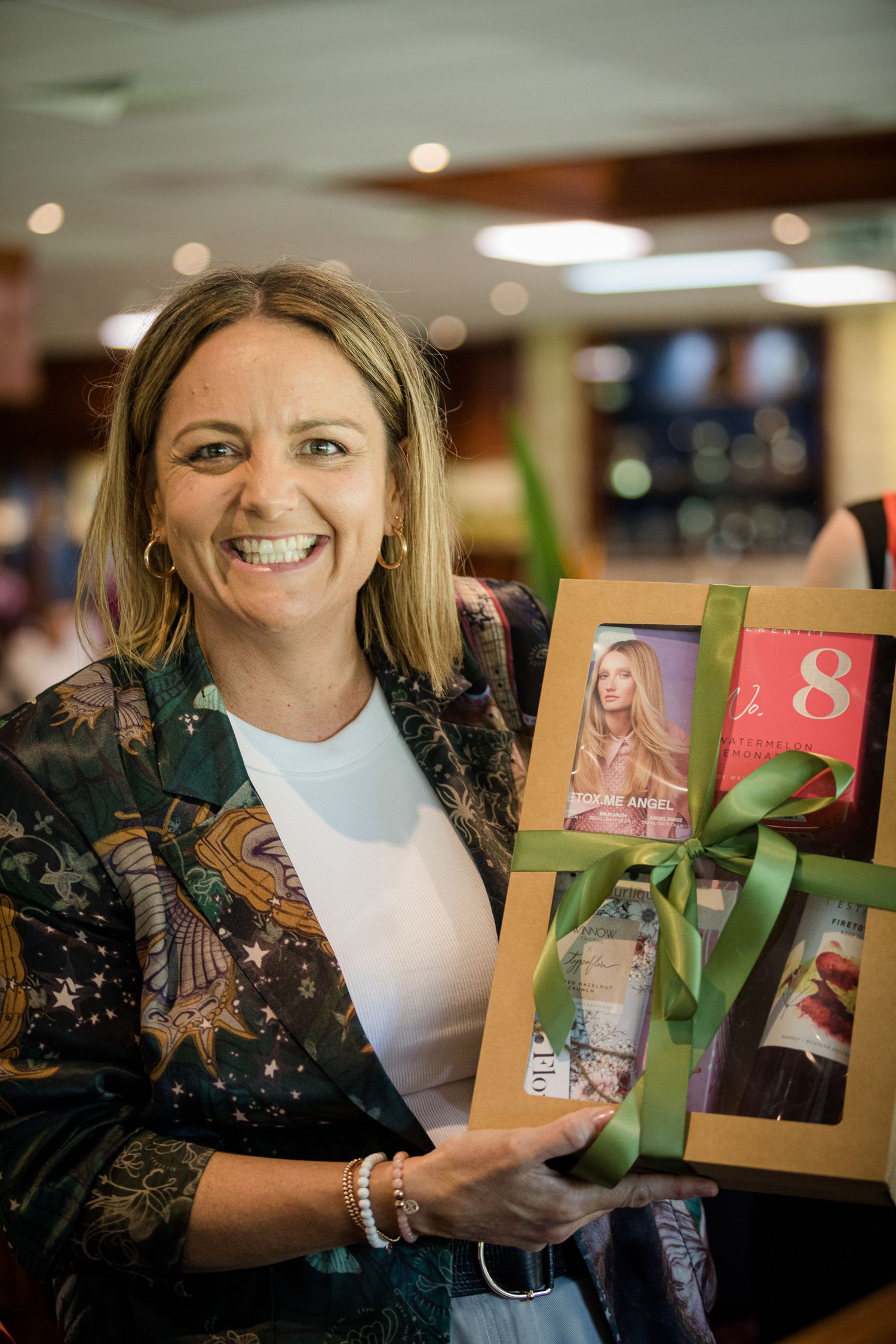 Someone holding a gift box with photos and decorative green ribbon in an indoor setting.
