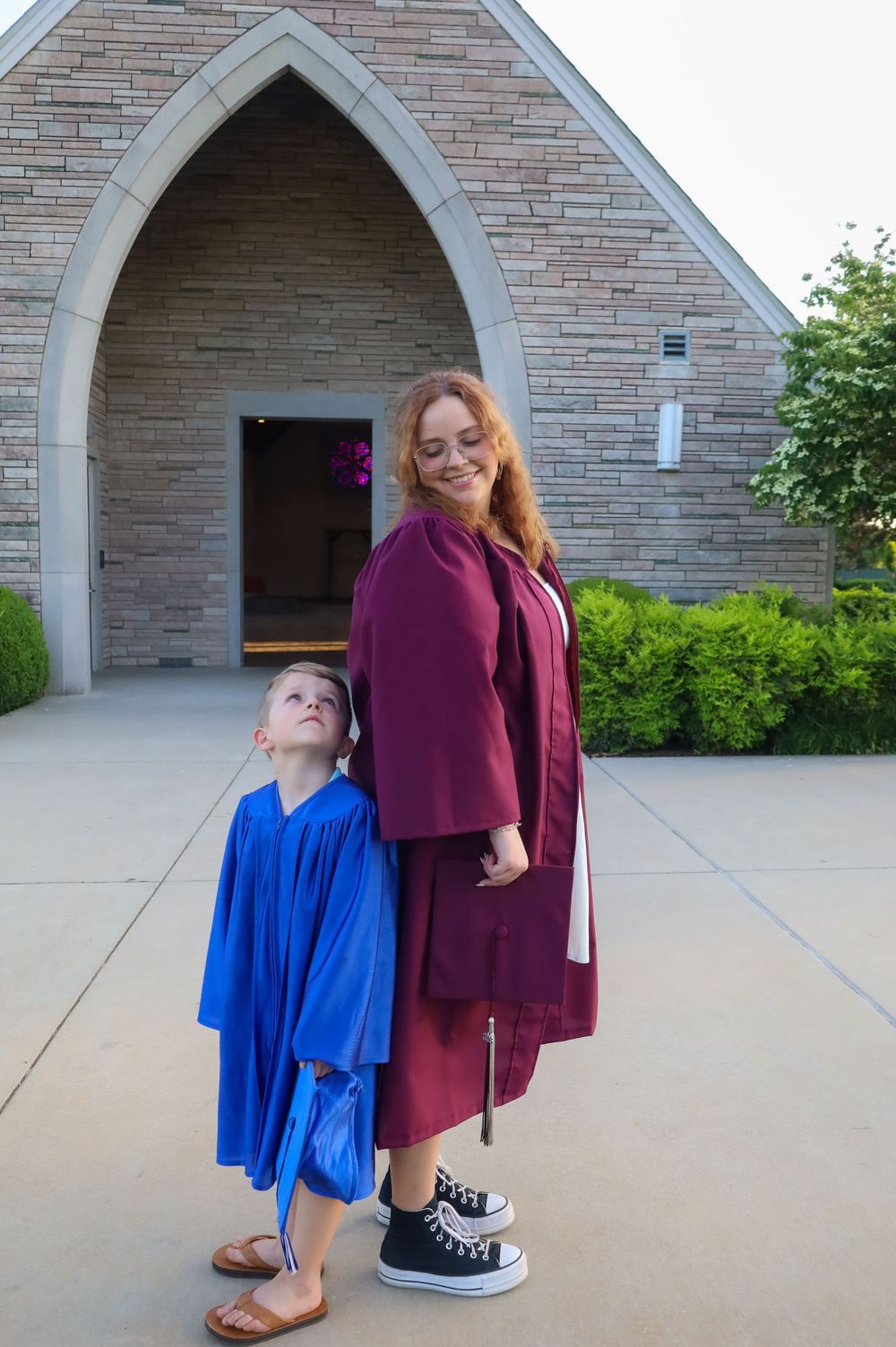 Two people in graduation attire posing in front of stone church archway.
