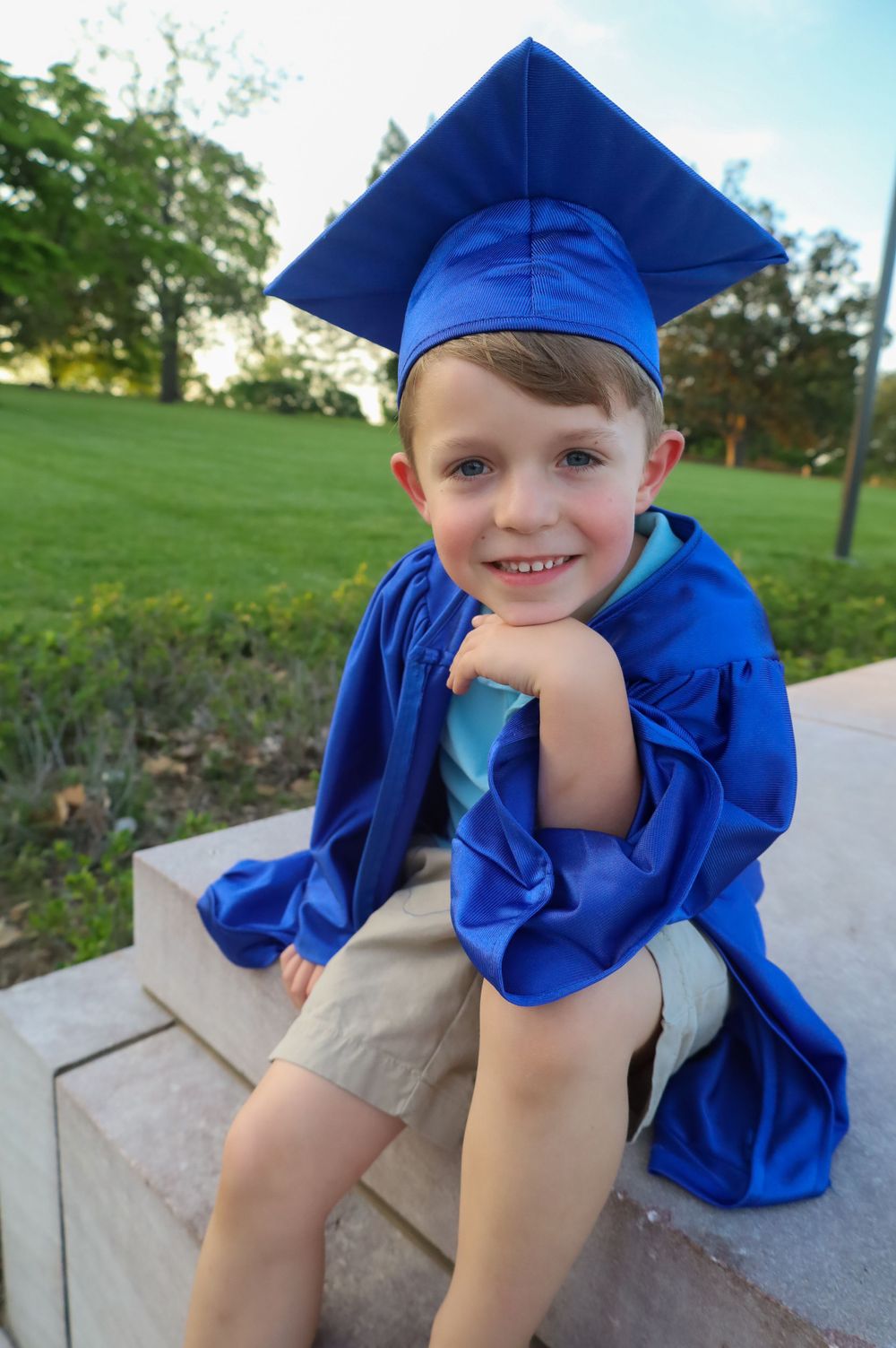 Child in bright blue graduation cap posing on outdoor steps.