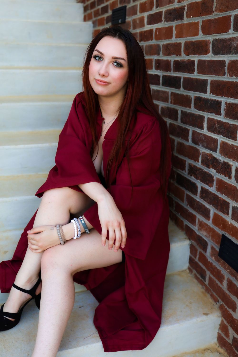 Person in burgundy wrap dress sitting on concrete steps against brick wall.