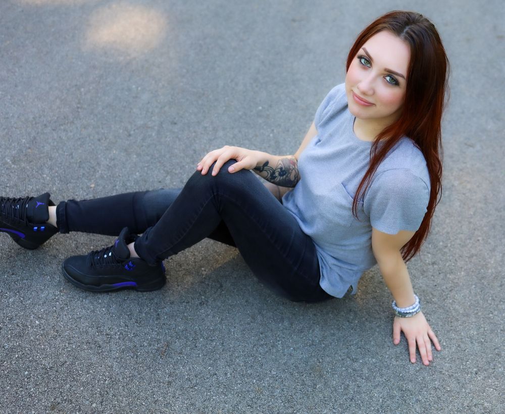 Person in gray shirt and jeans sitting on pavement.