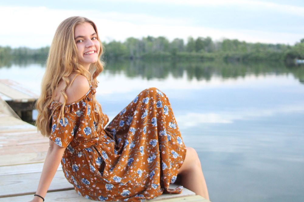 Woman in floral dress poses by lakeside during golden hour photoshoot.