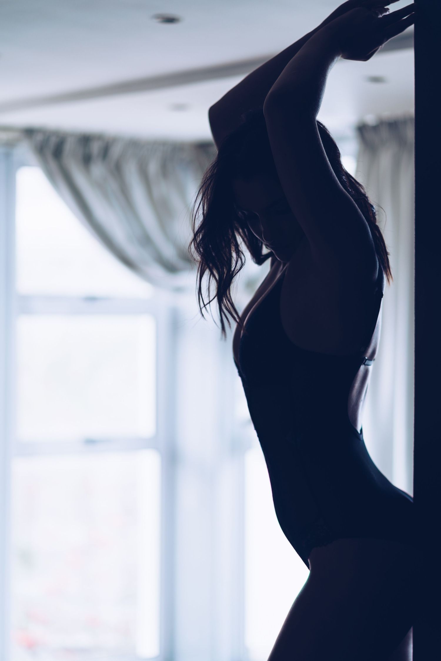 Artistic silhouette of a woman posing gracefully by a bright window in a dark room.