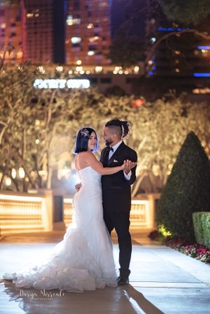 Couple shares romantic dance moment in elegant wedding attire against illuminated city backdrop.