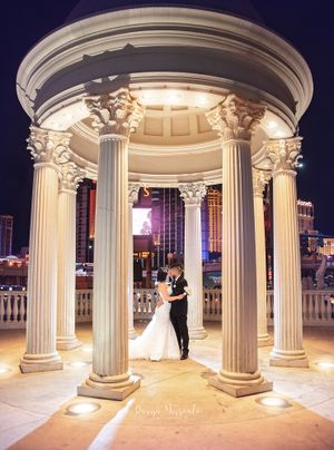 Wedding couple dances under ornate classical columned gazebo lit dramatically at night.