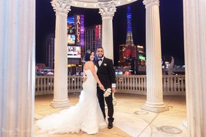 Wedding couple posing between elegant white columns with Las Vegas lights illuminating the background.