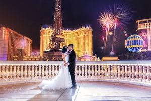 Wedding couple silhouetted against Las Vegas strip with fireworks bursting behind Paris hotel.