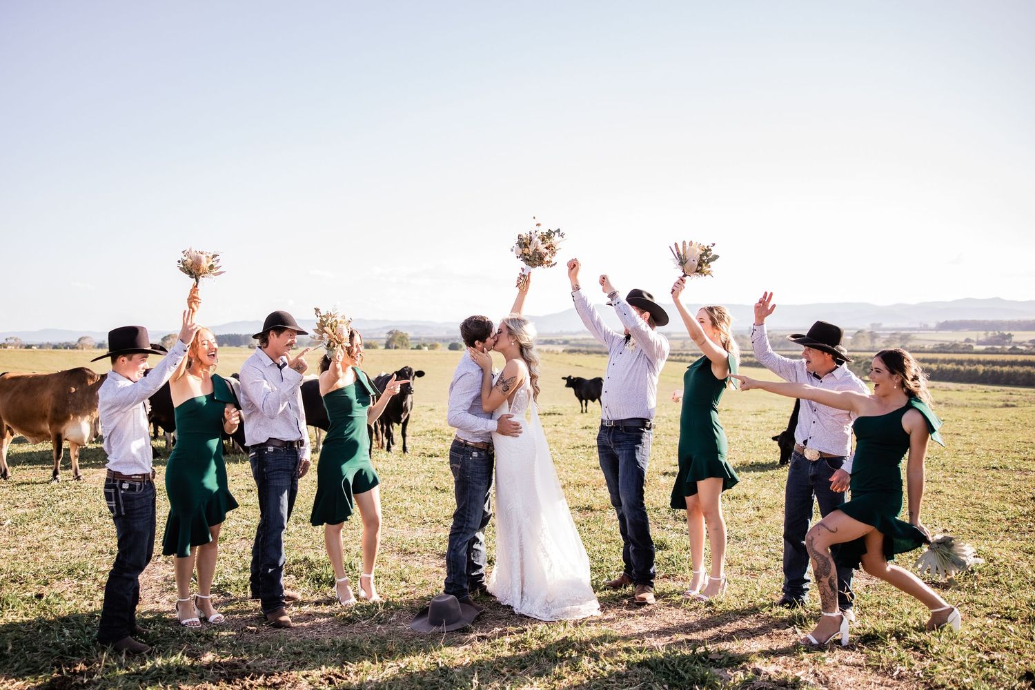 Bridal party celebrates with a jump shot in an open field with mountains in background.