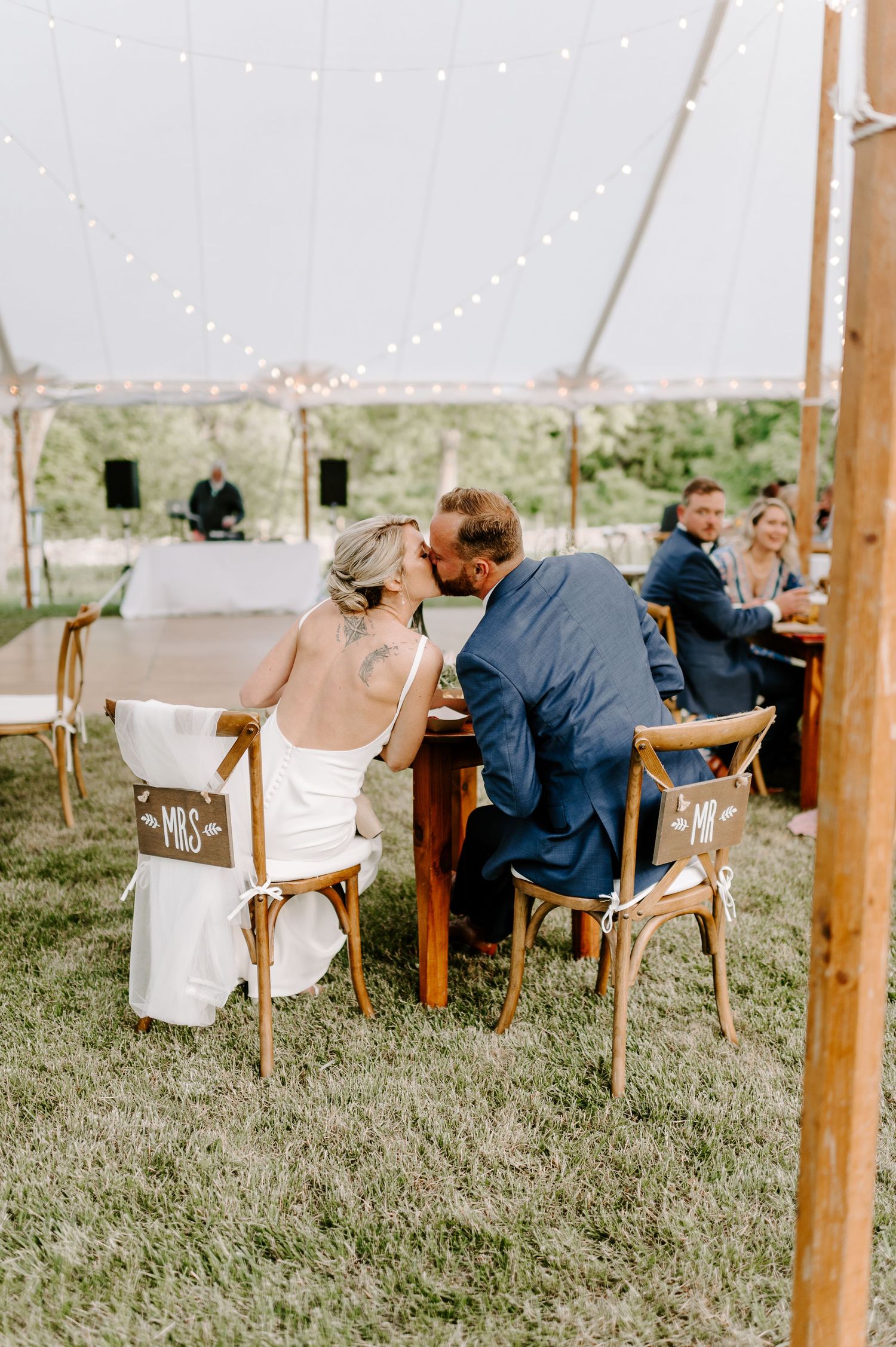 Outdoor wedding reception setup with wooden chairs under string lights on a grassy field.