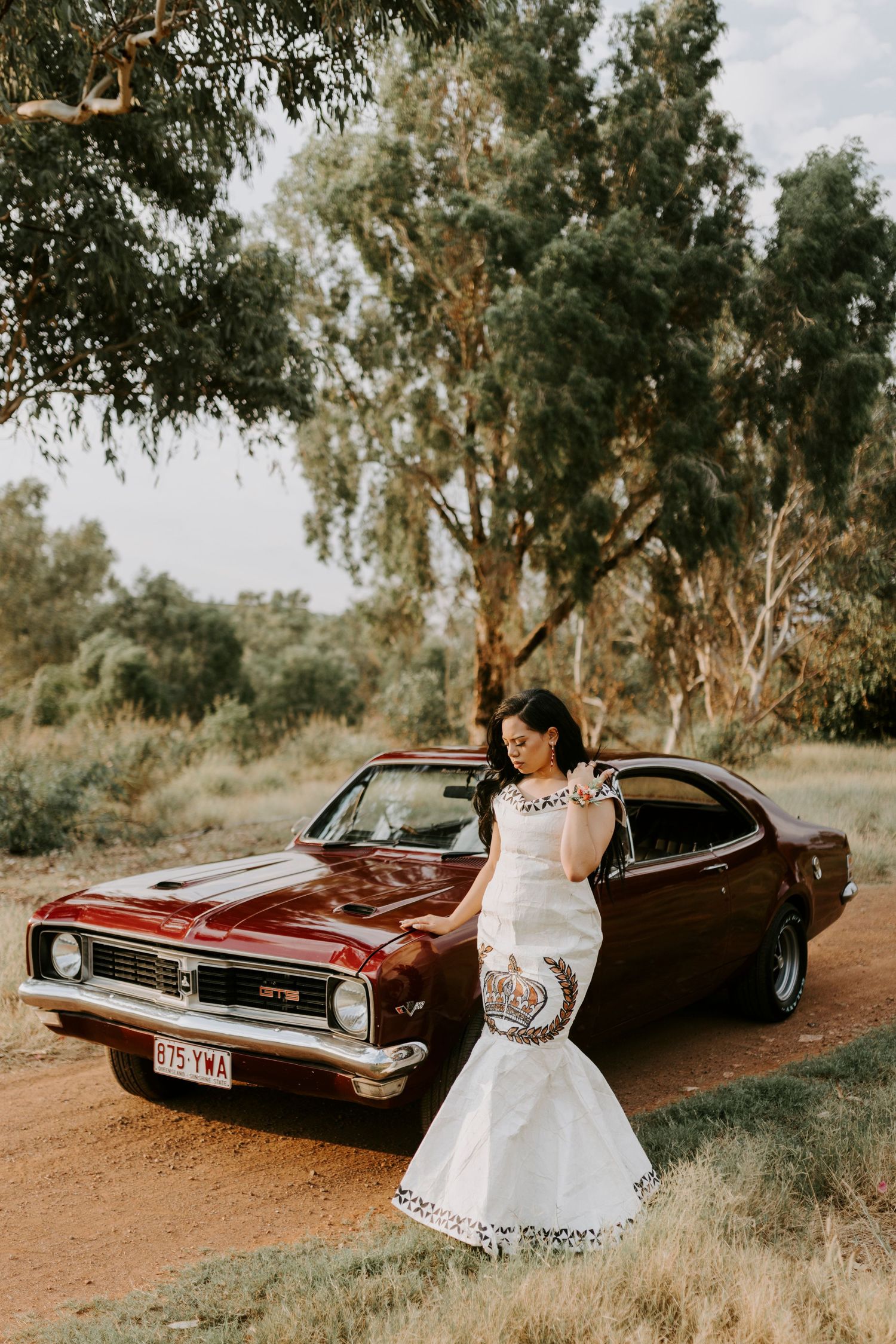 Woman leaning against a vintage car in Tongan cultural attire in Mount Isa