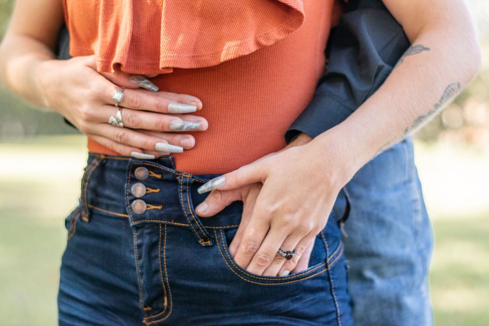 Detail shot of hands wearing rings against rust-colored top and denim jeans.