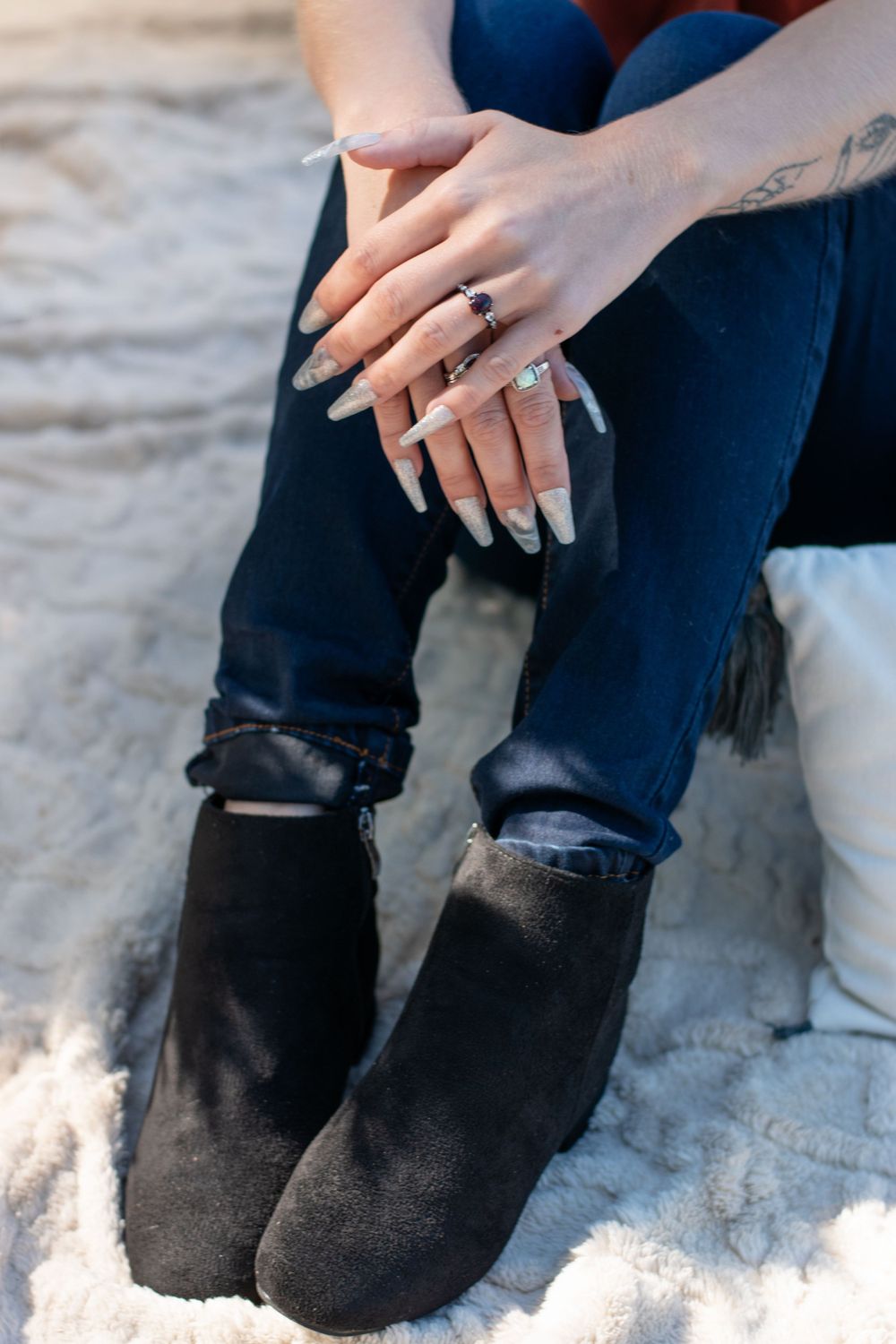 Close up of hands wearing multiple rings and black ankle boots against a light background.