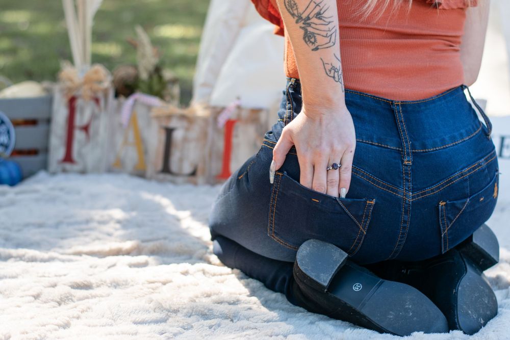 Close-up of person wearing blue jeans sitting on blanket with tattoo visible on arm.