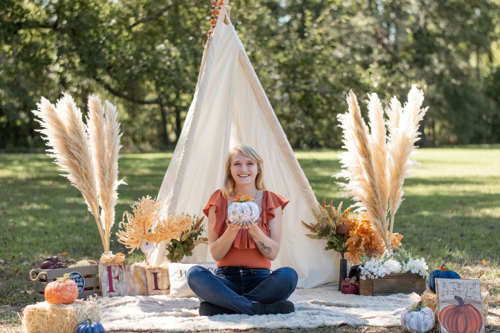 Lifestyle portrait with white teepee, pampas grass, and fall-themed decorations in outdoor setting.