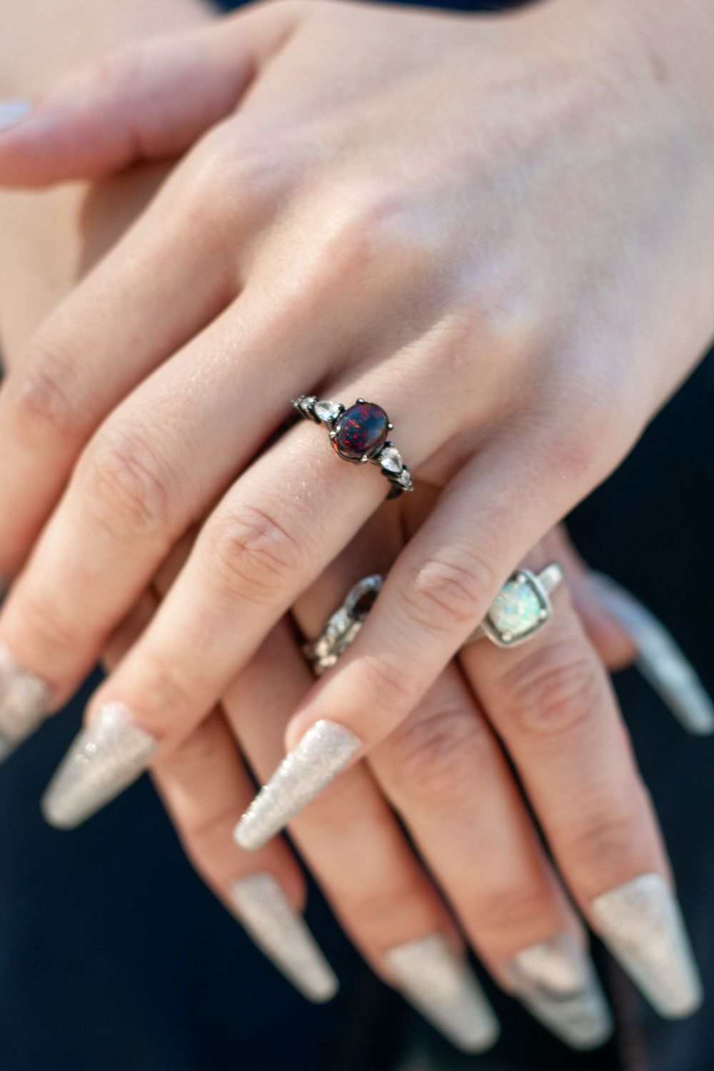 A detailed view of manicured hands wearing statement rings including a purple gemstone centerpiece.