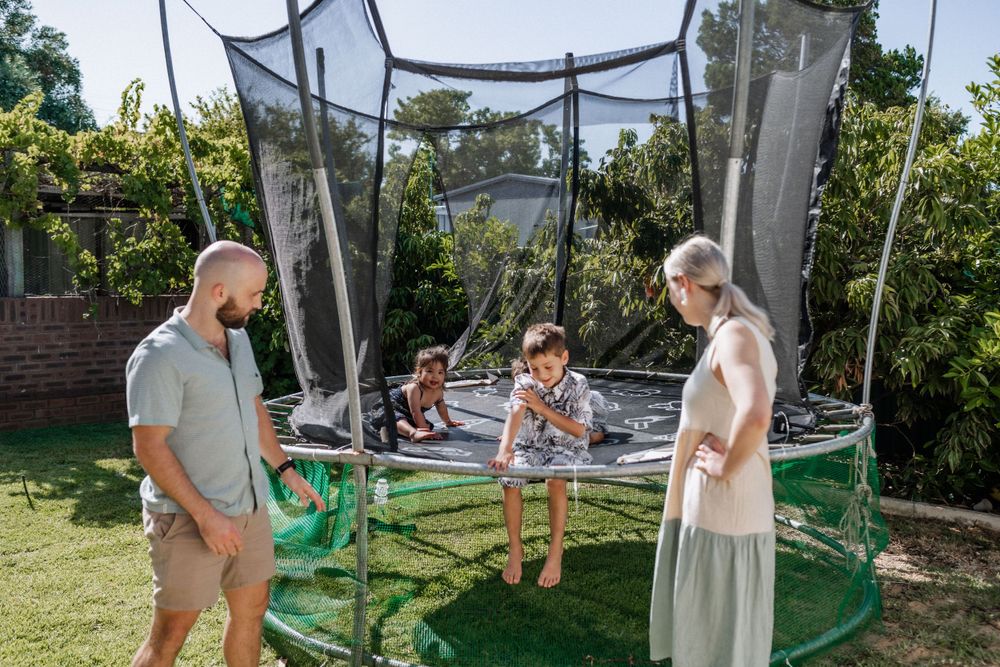Aunty, uncle and two nephews interacting on a trampoline in their backyard.
