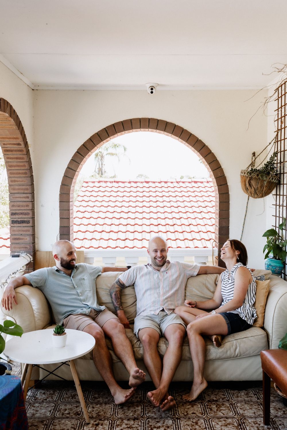 Three adult siblings laughing together on a couch during an extended family photo session