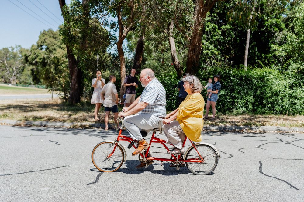 Grandparents riding a tandem bike together near their home