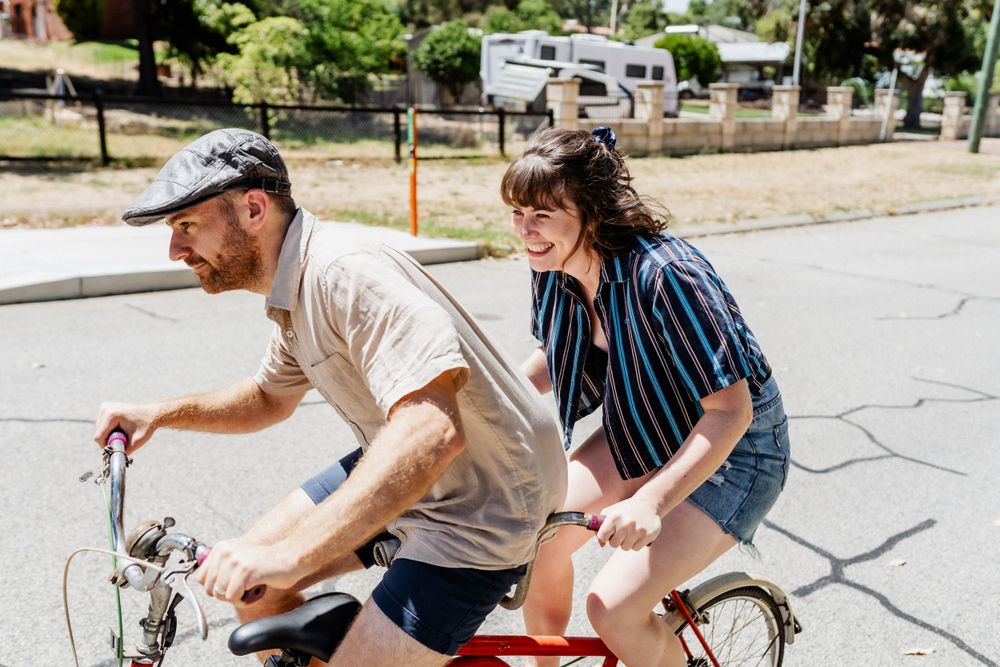 Two adult siblings riding a tandem bike together, laughing