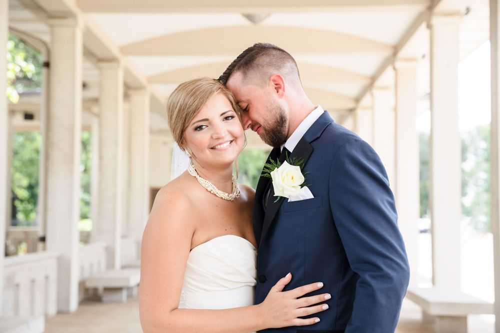 An intimate wedding portrait showing a tender moment under a white columned portico.