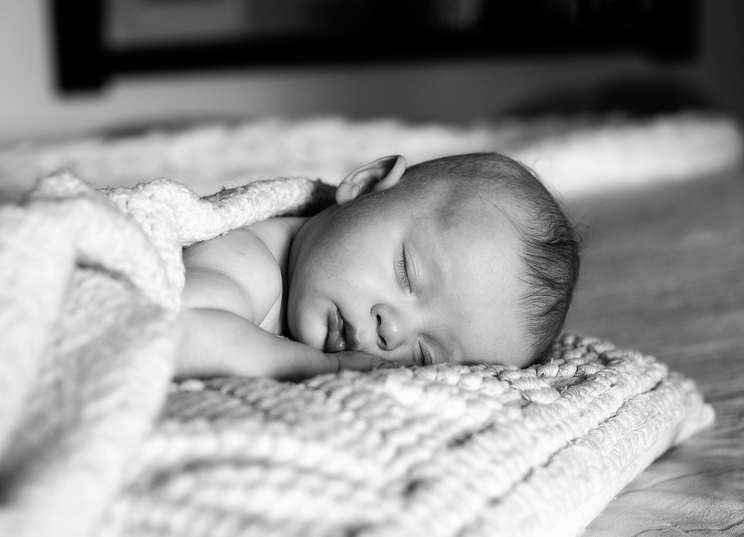 Black and white series of a sleeping newborn wrapped in textured blanket.
