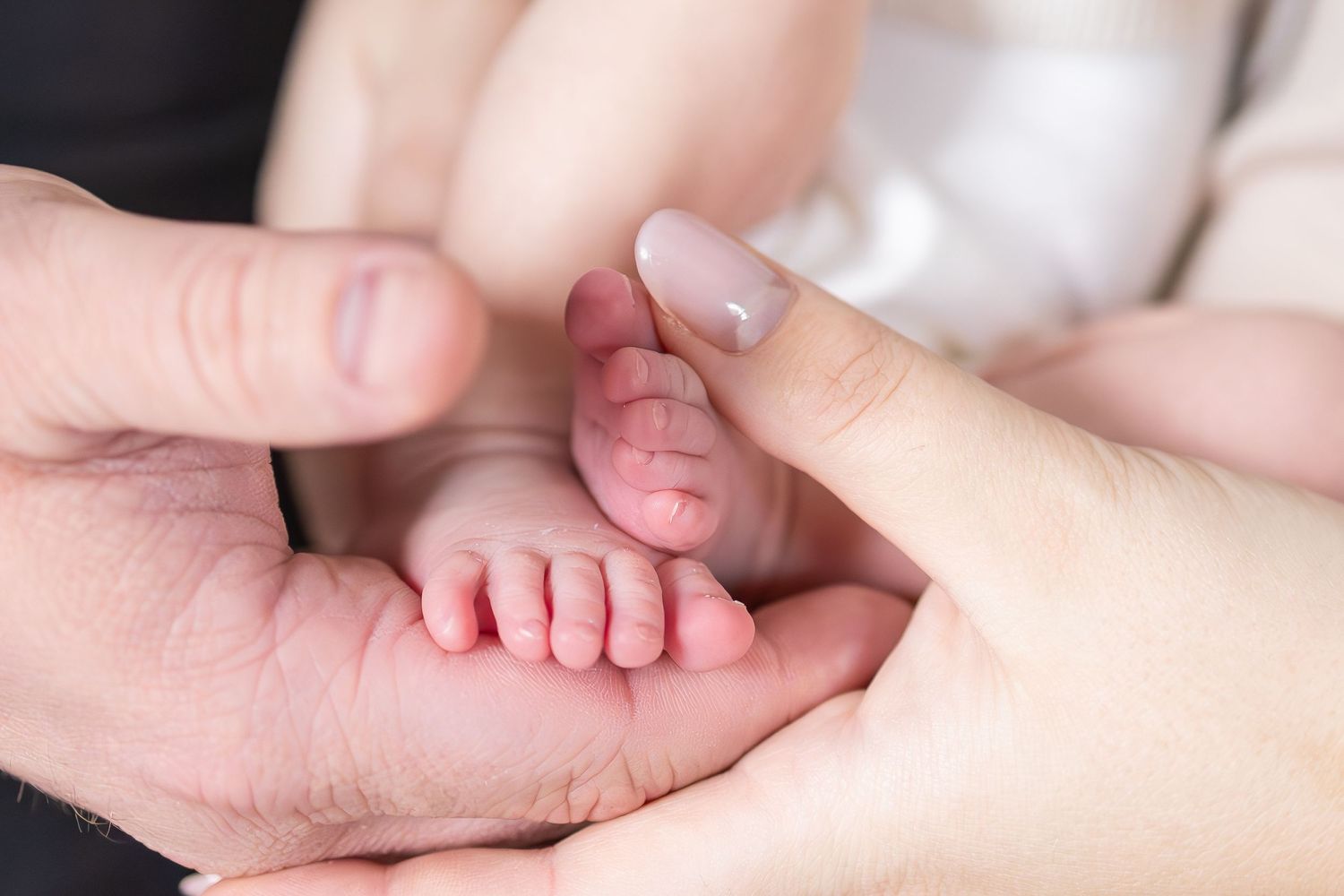 Tiny newborn baby feet being gently held in adult hands.